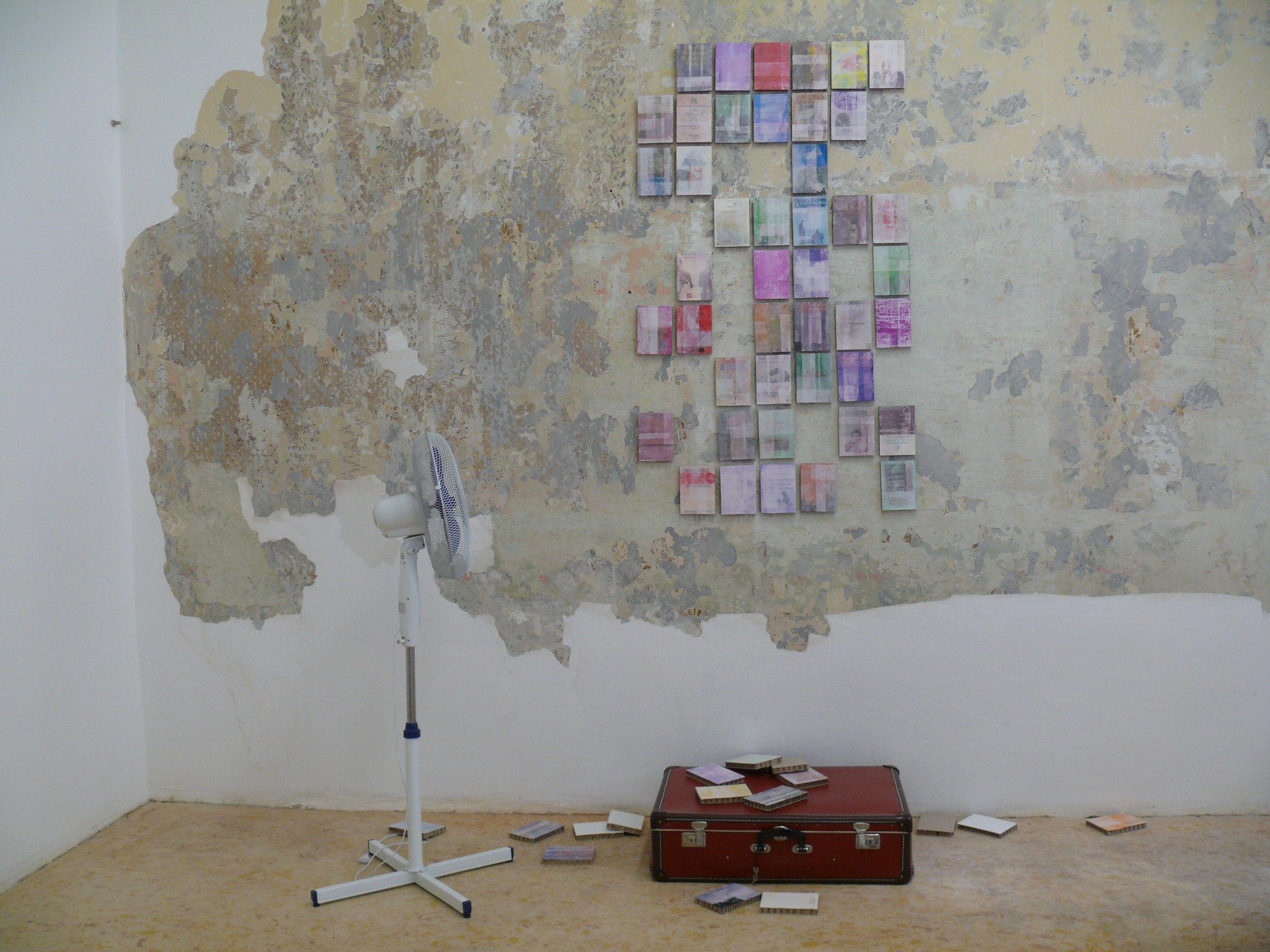 daimona aus dem koffer, installation view with wall-mounted cover paintings, suitcase and fan